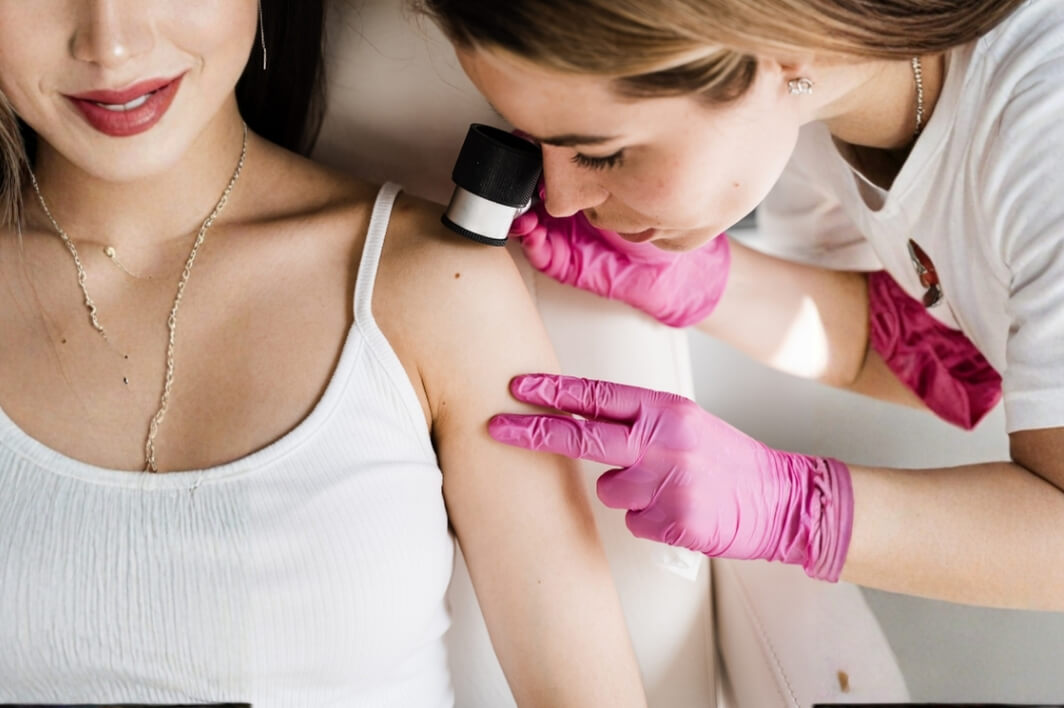 Dermatoszkópos anyajegy- és bőrvizsgálat rózsaszín kesztyűs szakemberrel a vállon